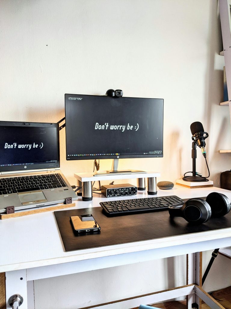 A desk with two screens that both say "don't worry be happy," along with a phone and headphones and a microphone